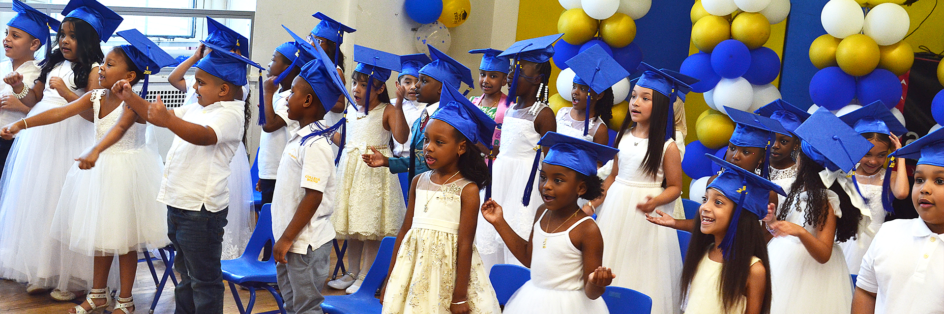 Children wearing graduation-style sashes, smiling.